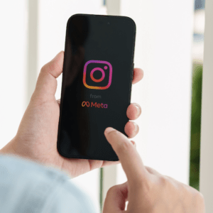 Caucasian female hand holding a smartphone with the Instagram logo displayed on a black background.