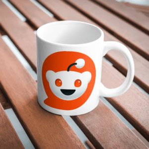 Photo of a white mug with the Reddit logo on it, sitting on a wooden table top.