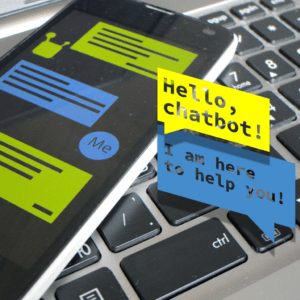 A smartphone rests on a keyboard. On the smartphone screen there is an outline of a chatbot chat, with the words "hello chatbot!" and "I am here to help" popping out in chat bubbles